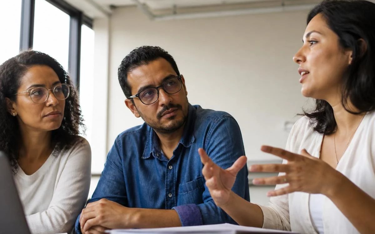 Roda de conversa numa sala clara, com uma pessoa expondo o ponto e duas escutando